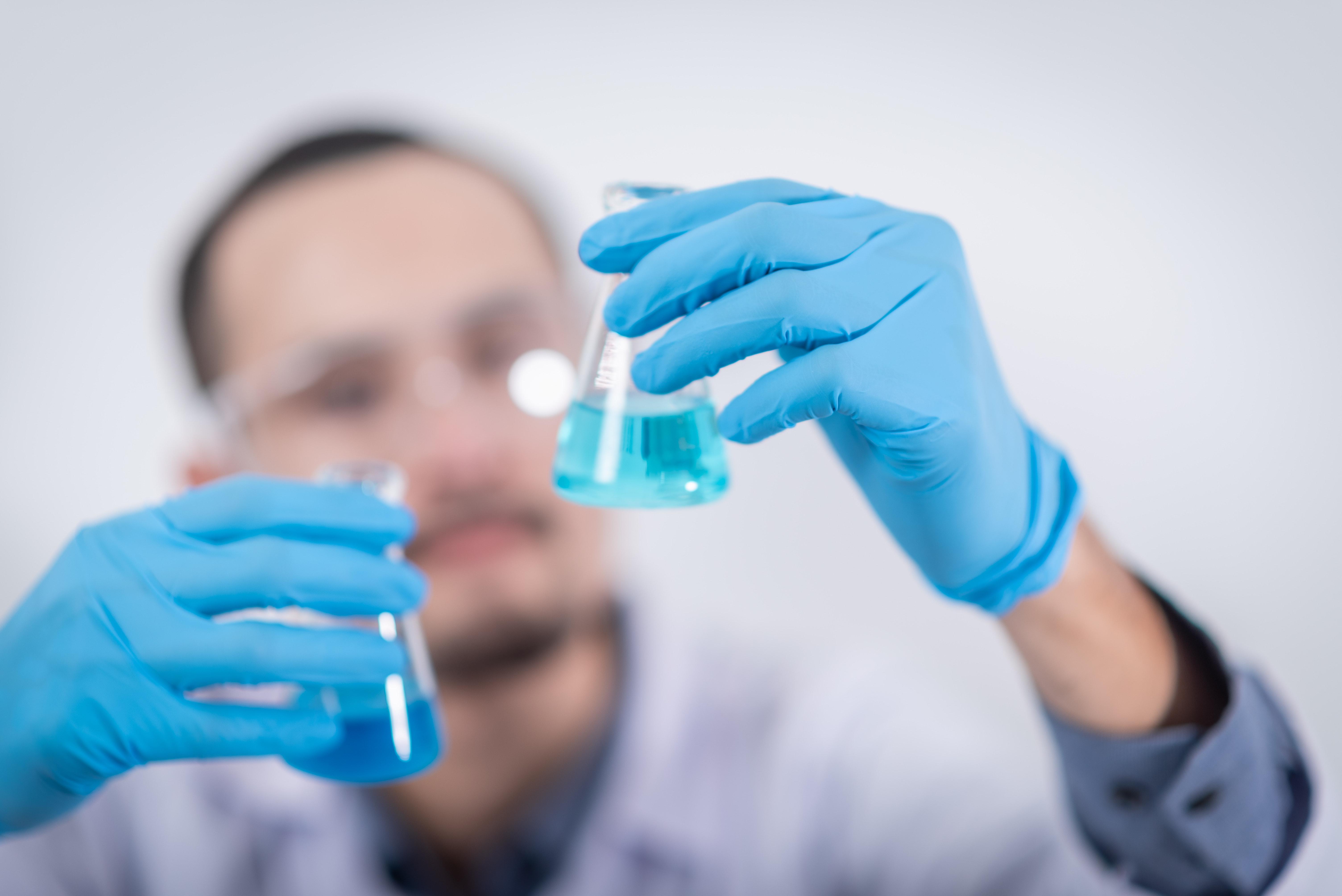 A male scientist holding two chemical flasks